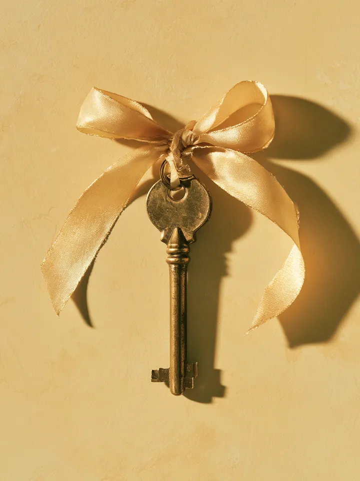 Brass door key hanging from a pastel ribbon, symbolizing the requirements that unlock a Happy Money loan