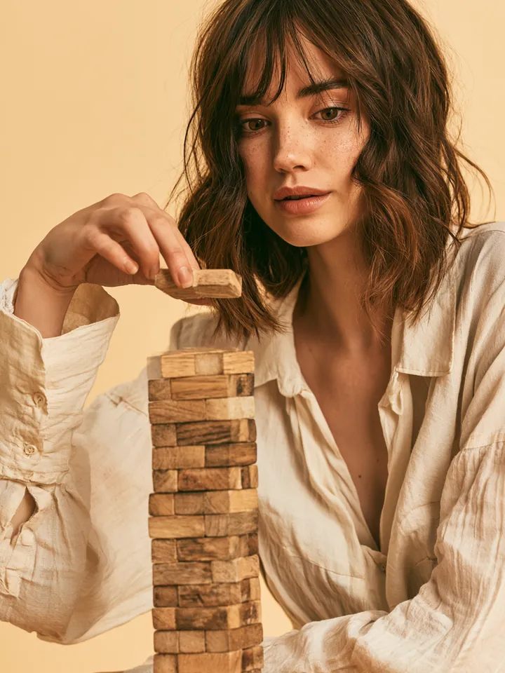 Woman placing a wooden block onto an even tower, symbolizing steady installment payments on a Happy Money loan
